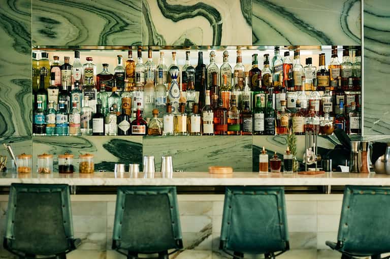 Luxury bar with green marbled backdrop, extensive spirit bottle collection, and emerald green bar seating