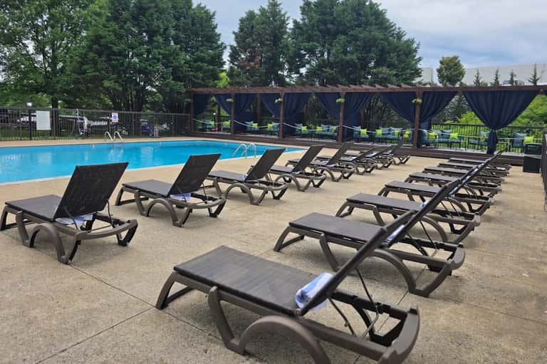 Large outdoor swimming pool with black loungers, white umbrellas, pergola shade structures, and mountain views