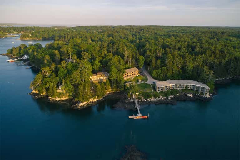 Aerial view of waterfront resort surrounded by dense forest on rocky peninsula with dock