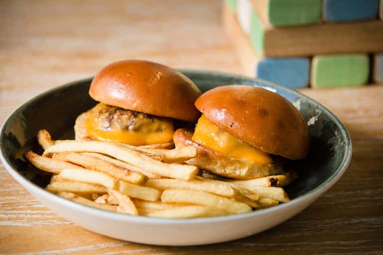 Two gourmet cheeseburgers with fries served on a dark plate