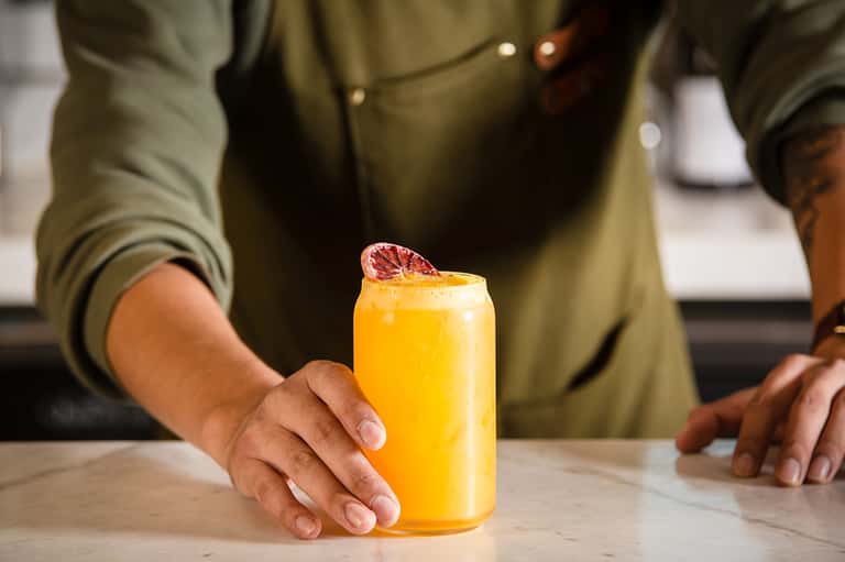 Person in olive shirt holding a tall glass of fresh orange juice with grapefruit slice garnish