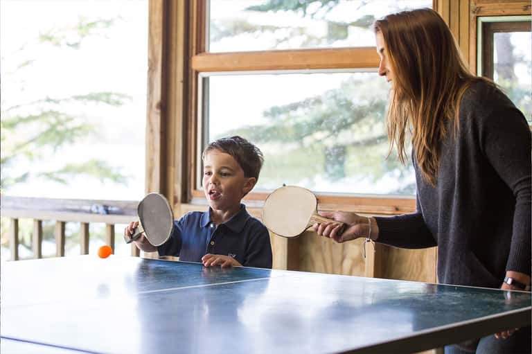 Woman and child playing table tennis indoors with mountain views through large windows