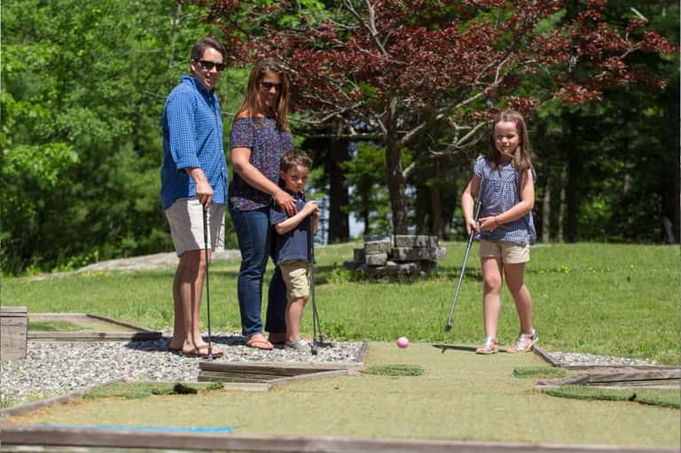 Family playing mini golf outdoors on a course with trees and natural landscape