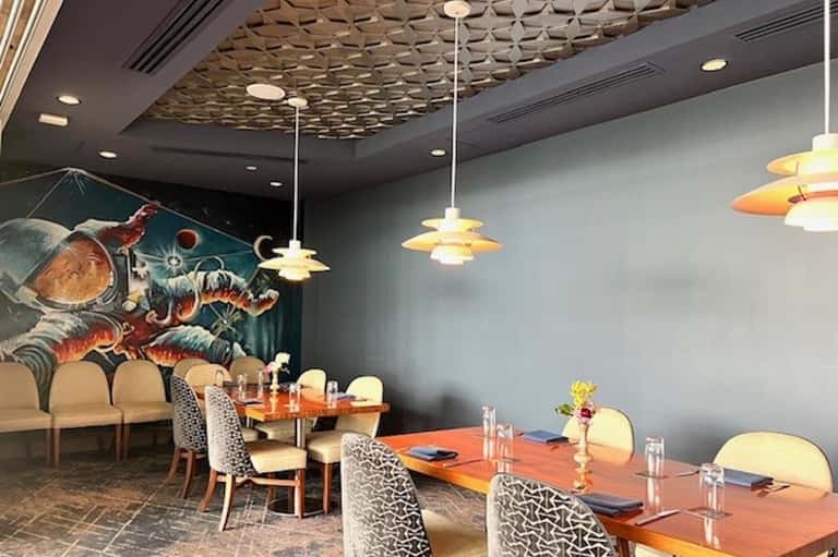 Modern dining room with geometric ceiling, pendant lights, wooden tables, and cosmic wall art mural