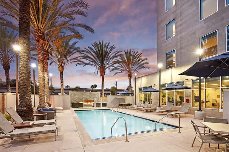 Illuminated resort pool at dusk with palm trees, lounge chairs, and modern building with lit windows