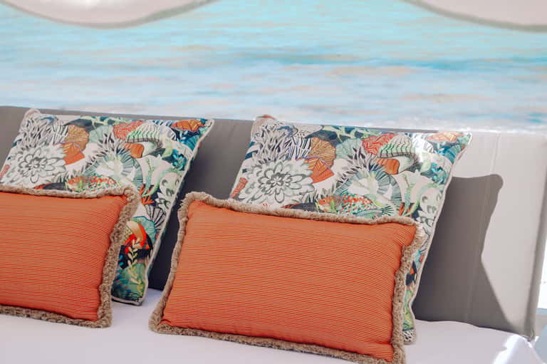 Luxury bedside pillows with colorful floral and orange striped patterns overlooking ocean view