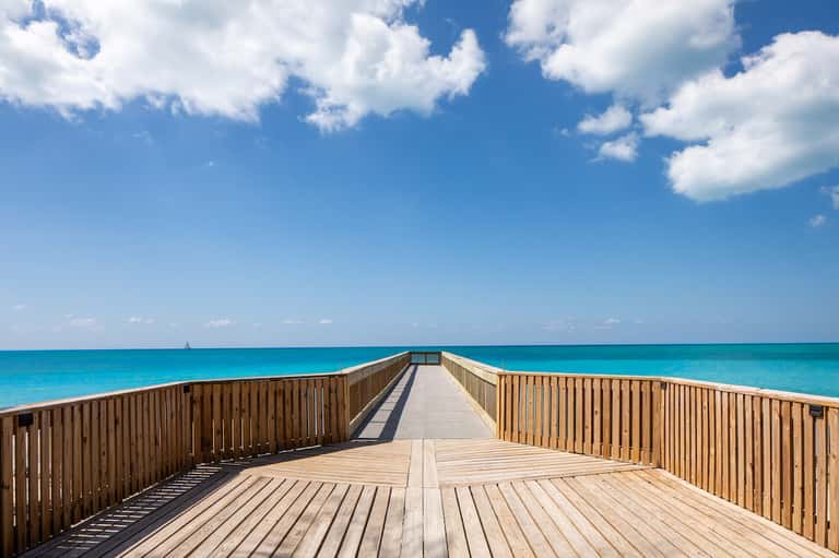 Wooden boardwalk pier extending over turquoise ocean water under blue sky