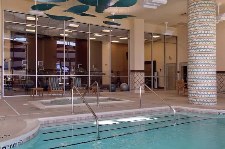 Indoor lap pool with lane dividers in modern hotel facility with glass walls and decorative ceiling elements