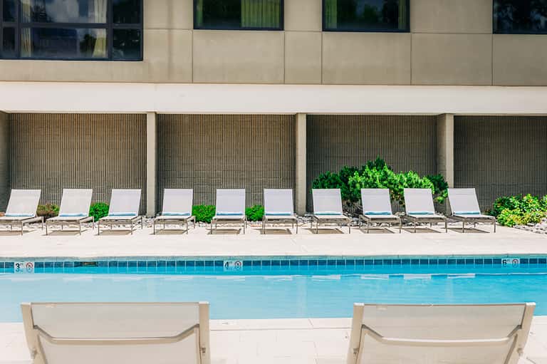Resort pool with white lounge chairs arranged along concrete deck and modern building backdrop