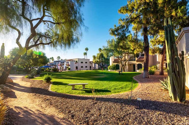 Desert resort grounds with manicured lawn, mature trees, and Southwestern-style architecture under blue sky