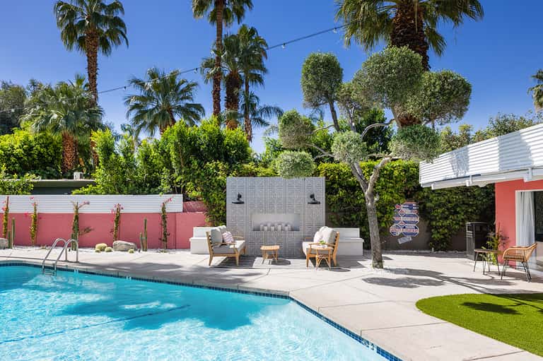 Resort pool area with lounge chairs, palm trees, fireplace feature wall, and clear blue water