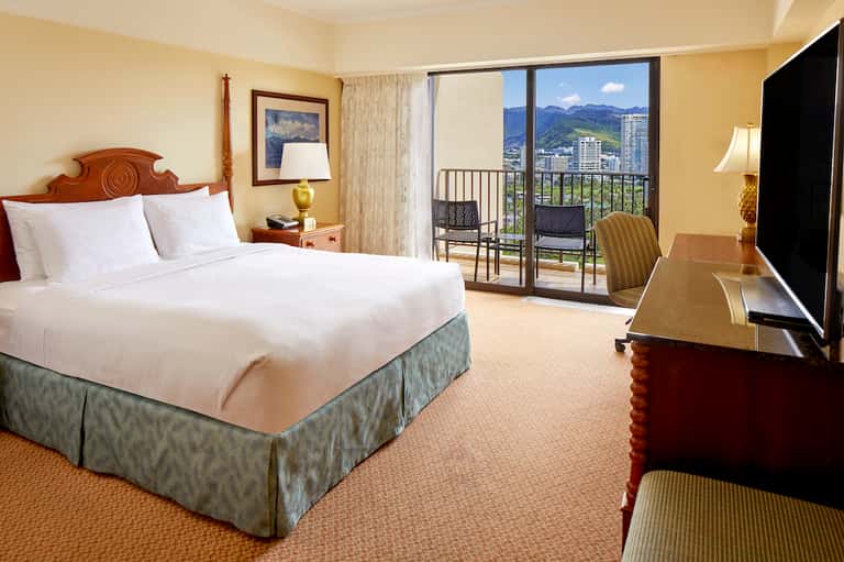 Upscale hotel bedroom with mountain view balcony, wooden bed frame, and flat-screen TV