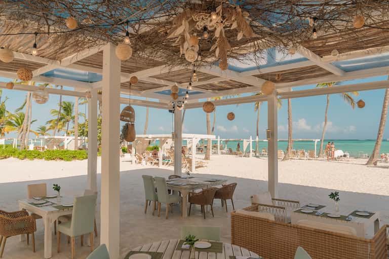 Modern beachfront dining pavilion with white columns and turquoise ocean backdrop