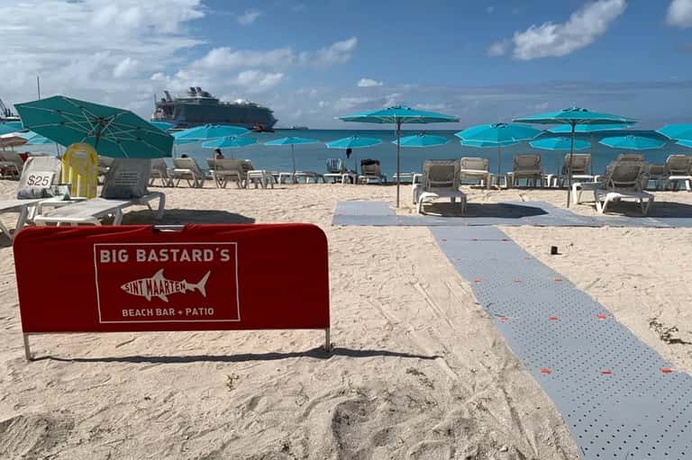 Beach club with turquoise umbrellas, lounge chairs, and a cruise ship in the distance
