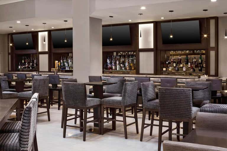 Modern bar lounge with dark wood cabinetry, pendant lighting, striped upholstered seating, and backlit shelves