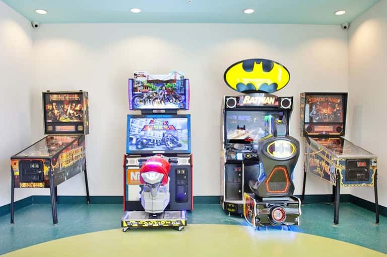 Game room with vintage pinball machines and Batman arcade game against white walls with blue ceiling