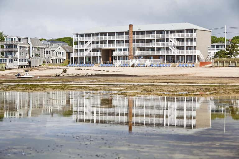 Beachfront hotel building with rows of blue loungers reflected in shallow water