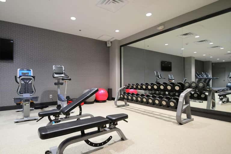Fitness center with cardio equipment, free weights, dumbbells, and large mirror wall