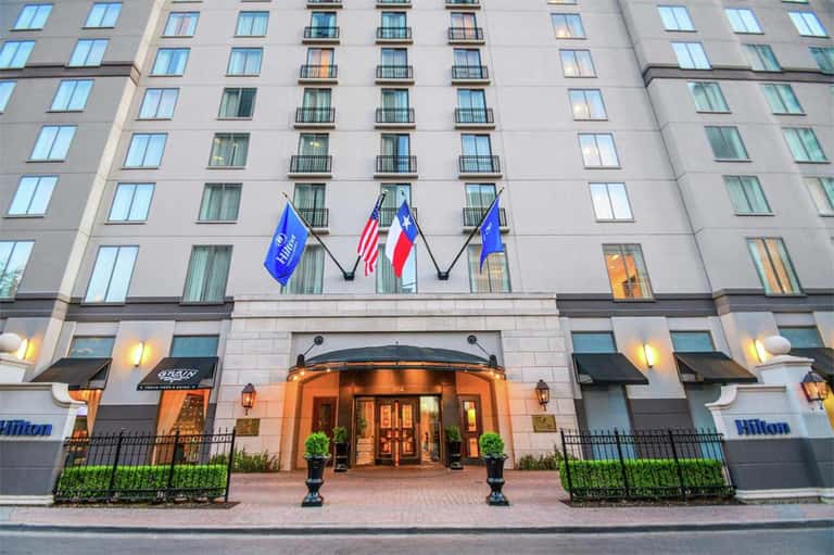 Hilton hotel entrance with elegant stone facade, flags, and manicured landscaping at dusk
