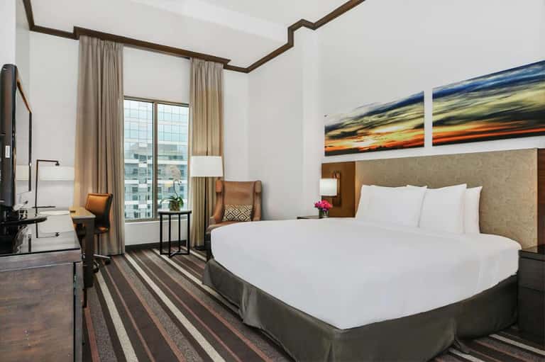 Modern hotel bedroom with king bed, work desk, and floor-to-ceiling windows with city views