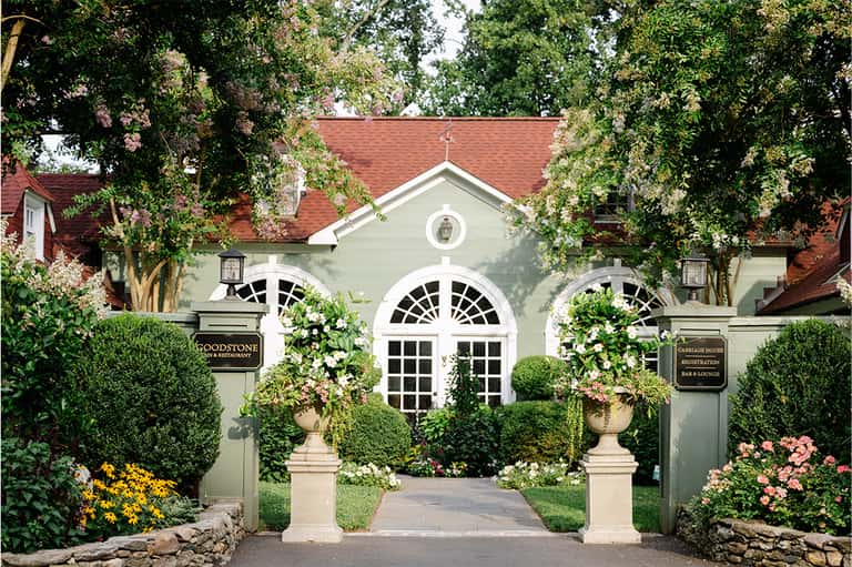 Elegant stone entrance to Goodstone Inn restaurant with arched windows, manicured hedges, and flowering planters