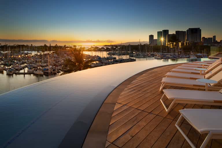 Waterfront infinity pool at sunset overlooking marina and city skyline