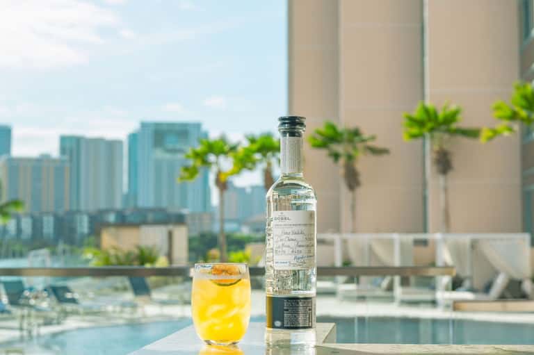 Cocktail with bottle on poolside table overlooking city skyline and palm trees