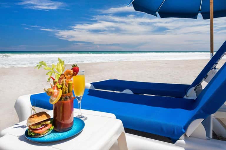 Beach lounge setup with blue chairs, umbrella, cocktails, and burger