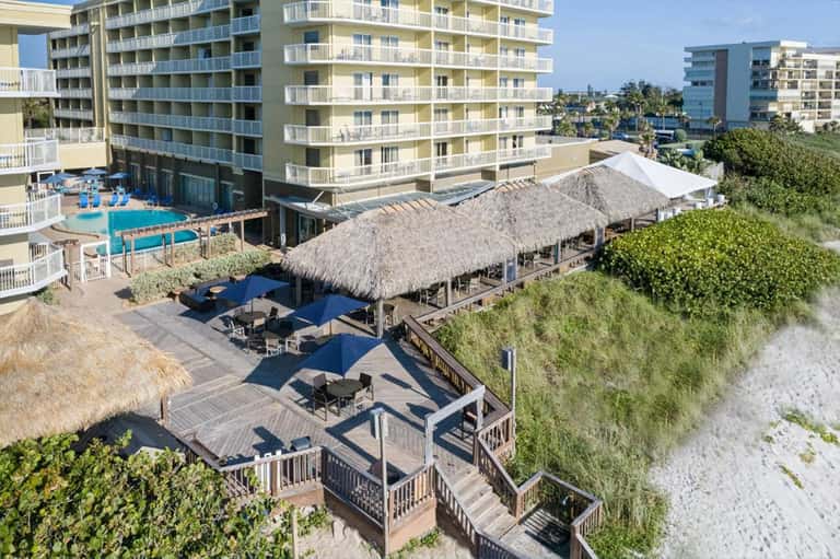 Beachfront resort aerial view with pool, tiki bar, deck seating, and sand access