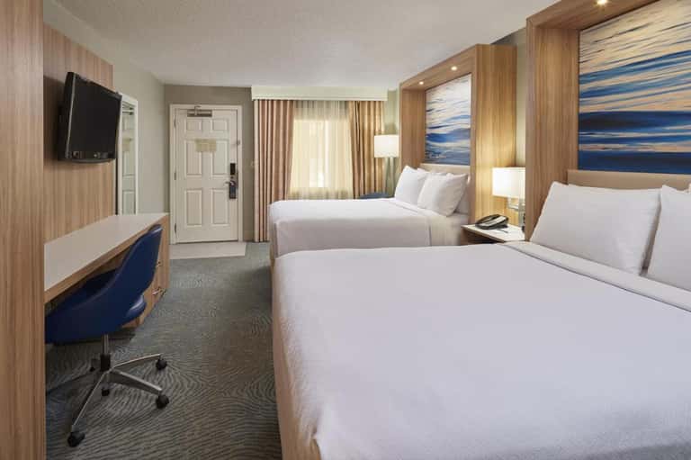 Modern hotel bedroom with two queen beds, wood accents, TV, and contemporary furnishings