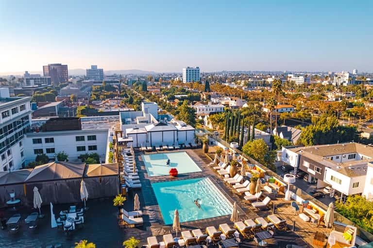 Aerial view of rooftop pool and lounging area overlooking a sprawling city landscape with mountains