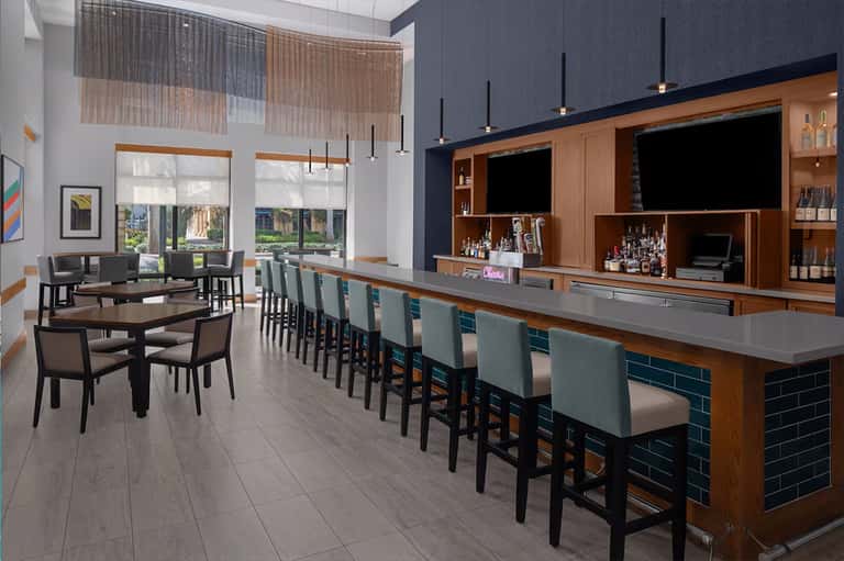 Modern hotel bar and lounge with wooden shelving, pendant lights, and high seating along a gray countertop