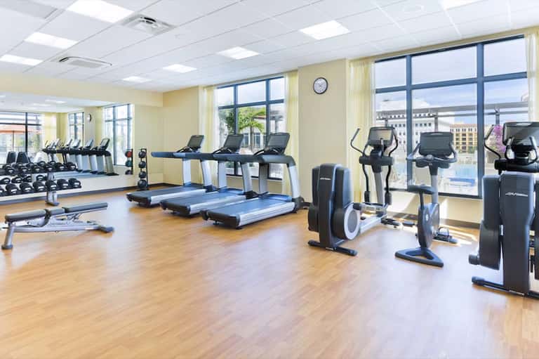 Modern fitness center with cardio equipment, treadmills, dumbbells, and floor-to-ceiling windows with city views