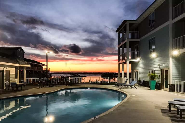 Lit swimming pool at dusk with waterfront view and dramatic sunset sky over buildings
