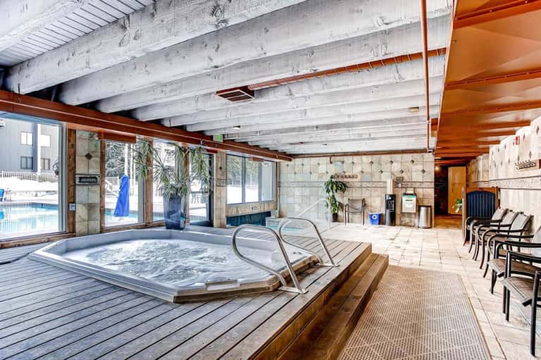 Indoor spa facility with hot tub, lounge chairs, and large windows overlooking outdoor pool area