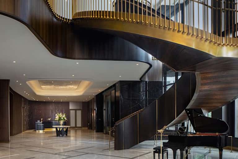Elegant spiral staircase with gold railings and grand piano in luxury hotel lobby