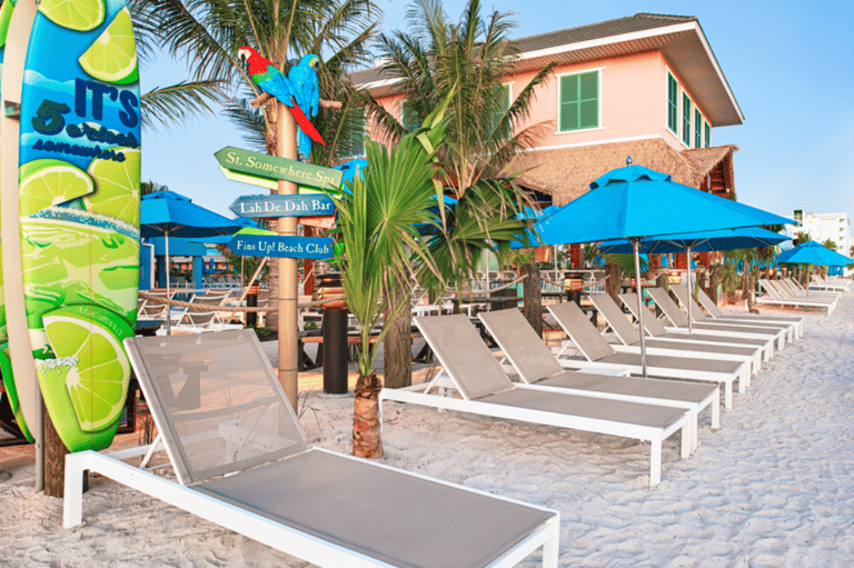 Colorful beach club with blue umbrellas, lounge chairs, palm trees, and tropical themed signage