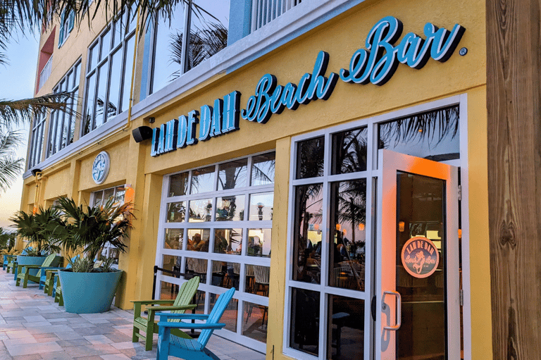 Tiki Beach Bar storefront with yellow exterior, blue signage, and colorful Adirondack chairs on patio