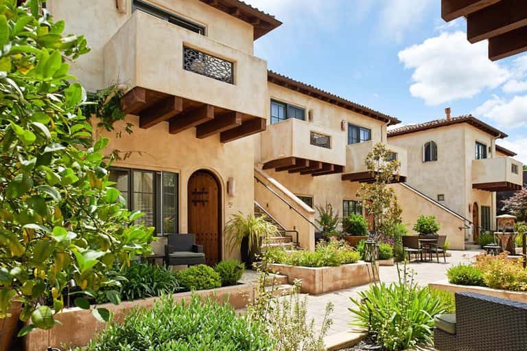 Tuscan-style resort courtyard with terracotta buildings, wooden doors, landscaped gardens, and outdoor seating