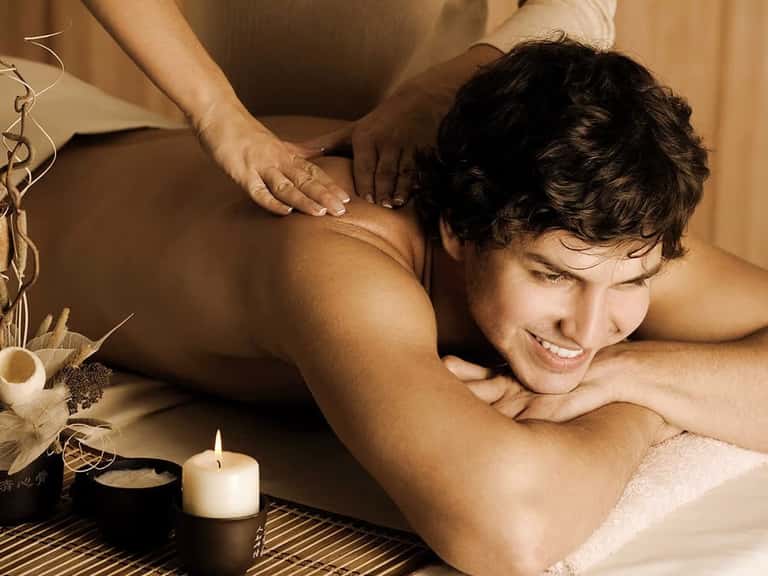 Man receiving professional massage therapy in spa setting with candles and natural décor
