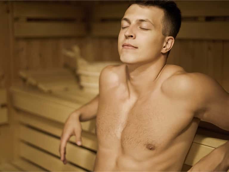 Man relaxing in sauna with wooden interior and closed eyes
