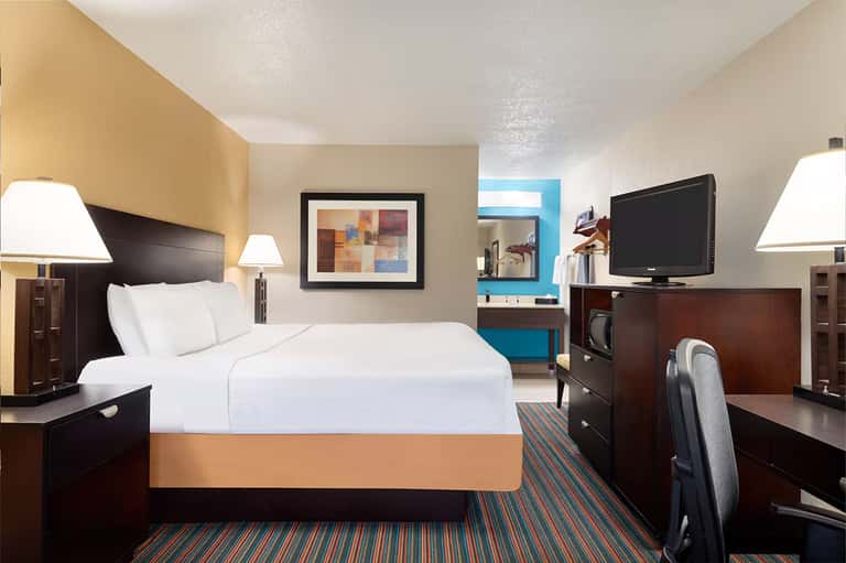 Modern hotel bedroom with dark wood furniture, white bedding, orange bed base, and flat-screen TV