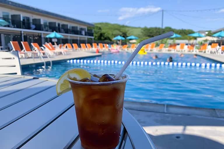 Cocktail with lime garnish on poolside lounge chair overlooking resort swimming pool with orange and blue loungers