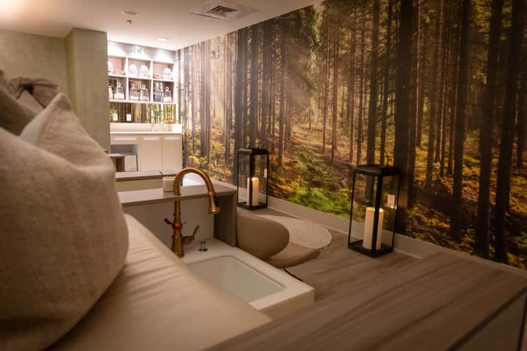 Luxury spa bathroom with soaking tub, forest mural wallpaper, and white shelving unit