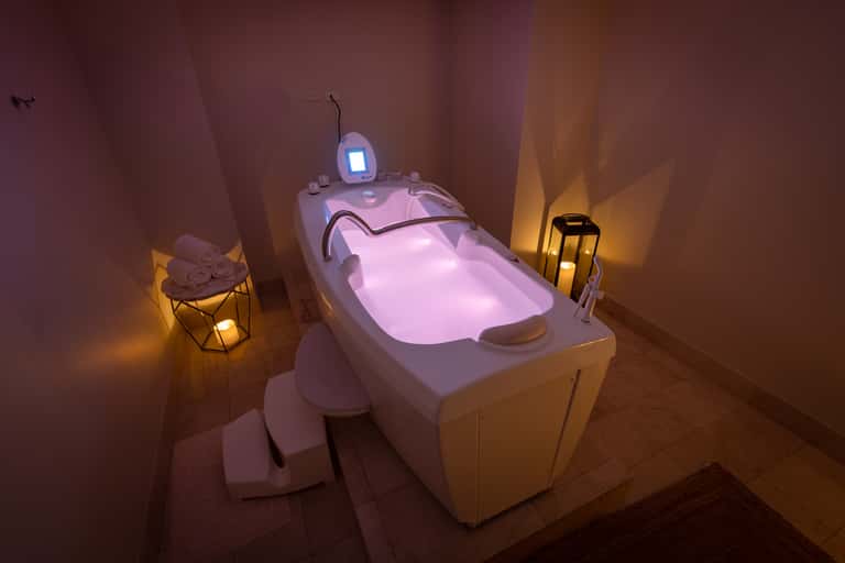 Spa treatment room with illuminated pink hydrotherapy tub, ambient lighting, and folded towels on side table