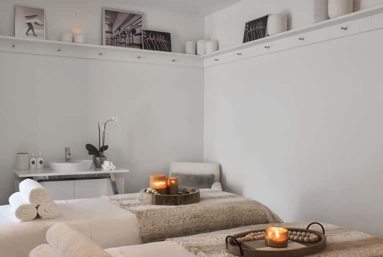 Serene spa treatment room with white linens, massage table, candles, and sink vanity