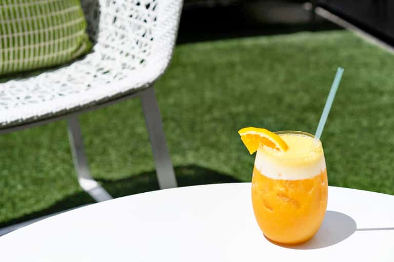 Orange cocktail with lemon slice on white table beside modern green and white patio chair