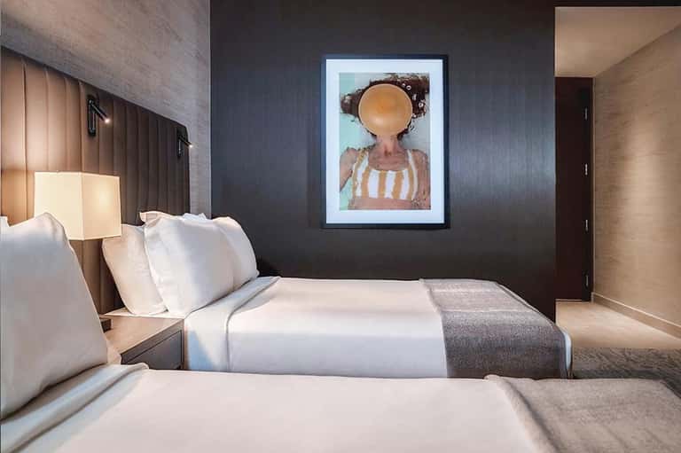 Modern hotel bedroom with two beds, dark accent wall, and framed artwork