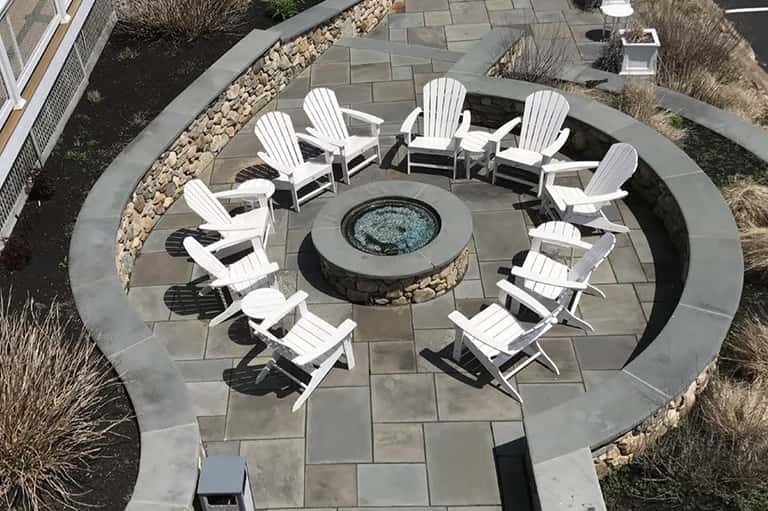 Overhead view of circular fire pit seating area with white Adirondack chairs on stone patio