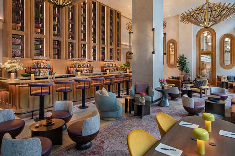 Upscale bar and lounge with wooden wine display, navy bar stools, colorful accent chairs, and architectural mirrors